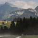 Green trees are seen in front of snow-capped mountains in the Alps.